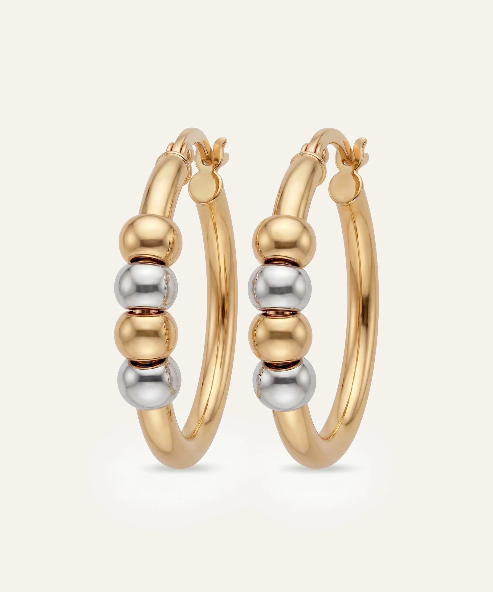Gold hoop earrings with bead detailing on a light beige background