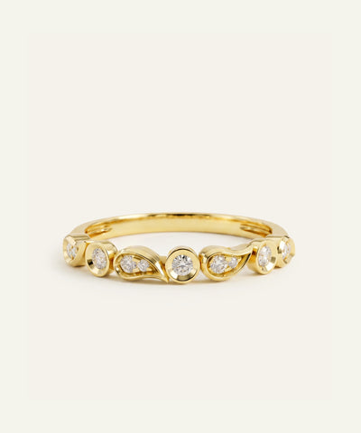 A yellow gold band ring featuring a series of wavy, leaf-like settings holding small clear round-cut gemstones, photographed on a clean, light off-white background. - alternate view