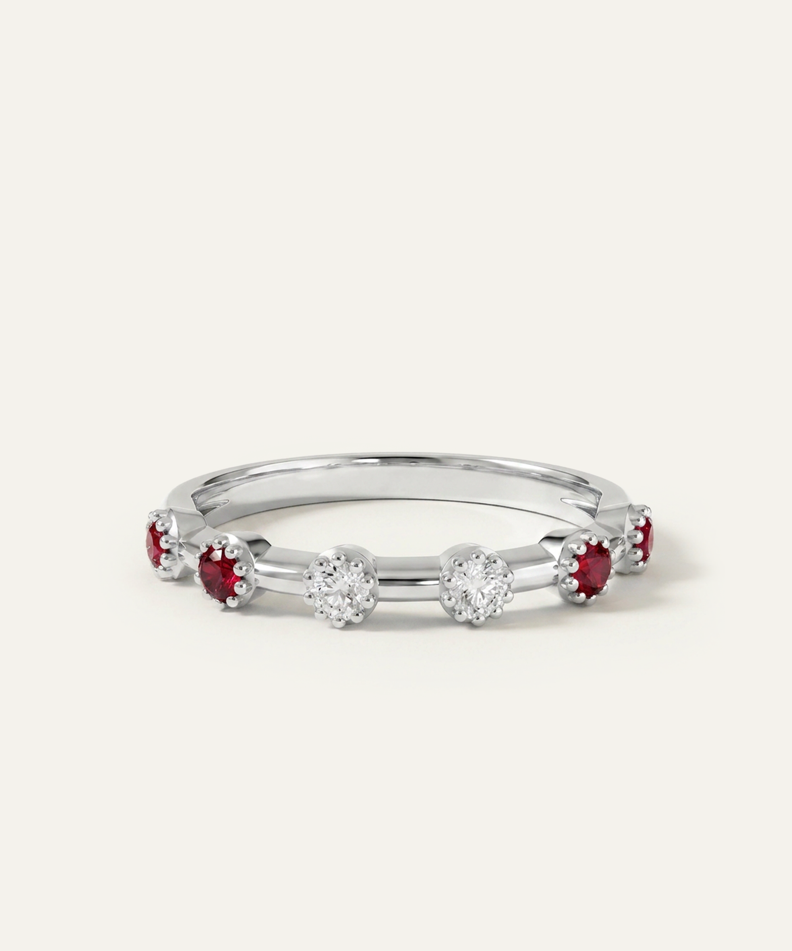 A silver band ring featuring alternating clusters of round-cut red gemstones and clear round-cut gemstones, photographed on a clean off-white background.