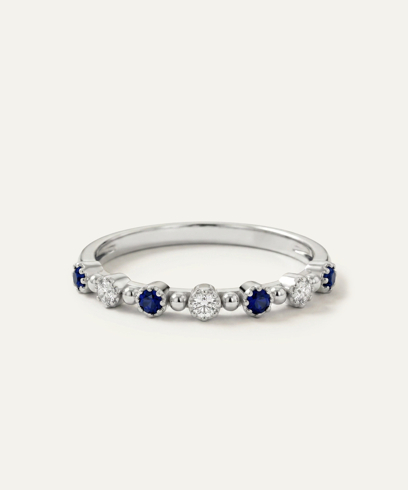 A silver-toned eternity ring featuring alternating round-cut deep blue sapphires and clear round diamonds, set against a clean off-white background.