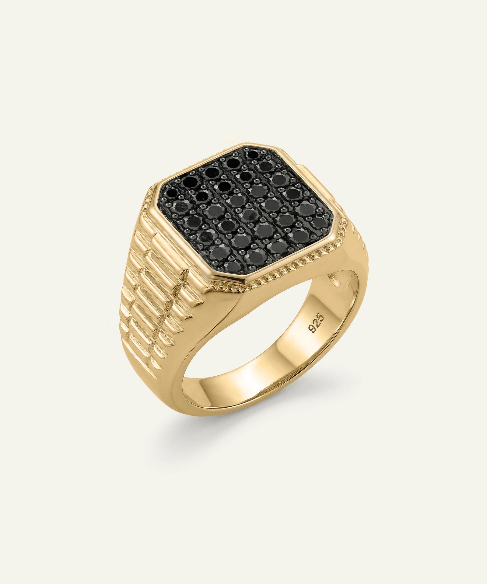 A gold signet ring with a black pavé face, photographed on a light off-white background.