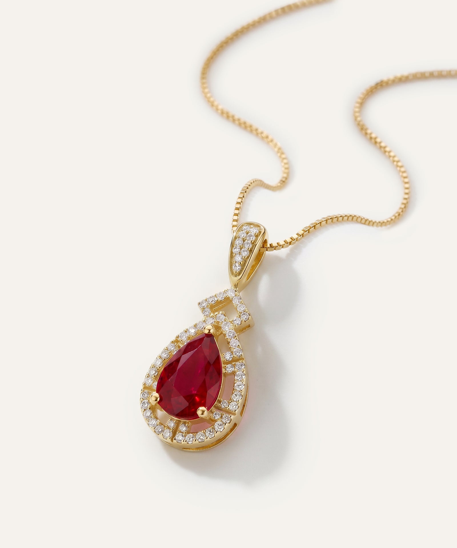 Gold necklace with a red gemstone pendant on a white background