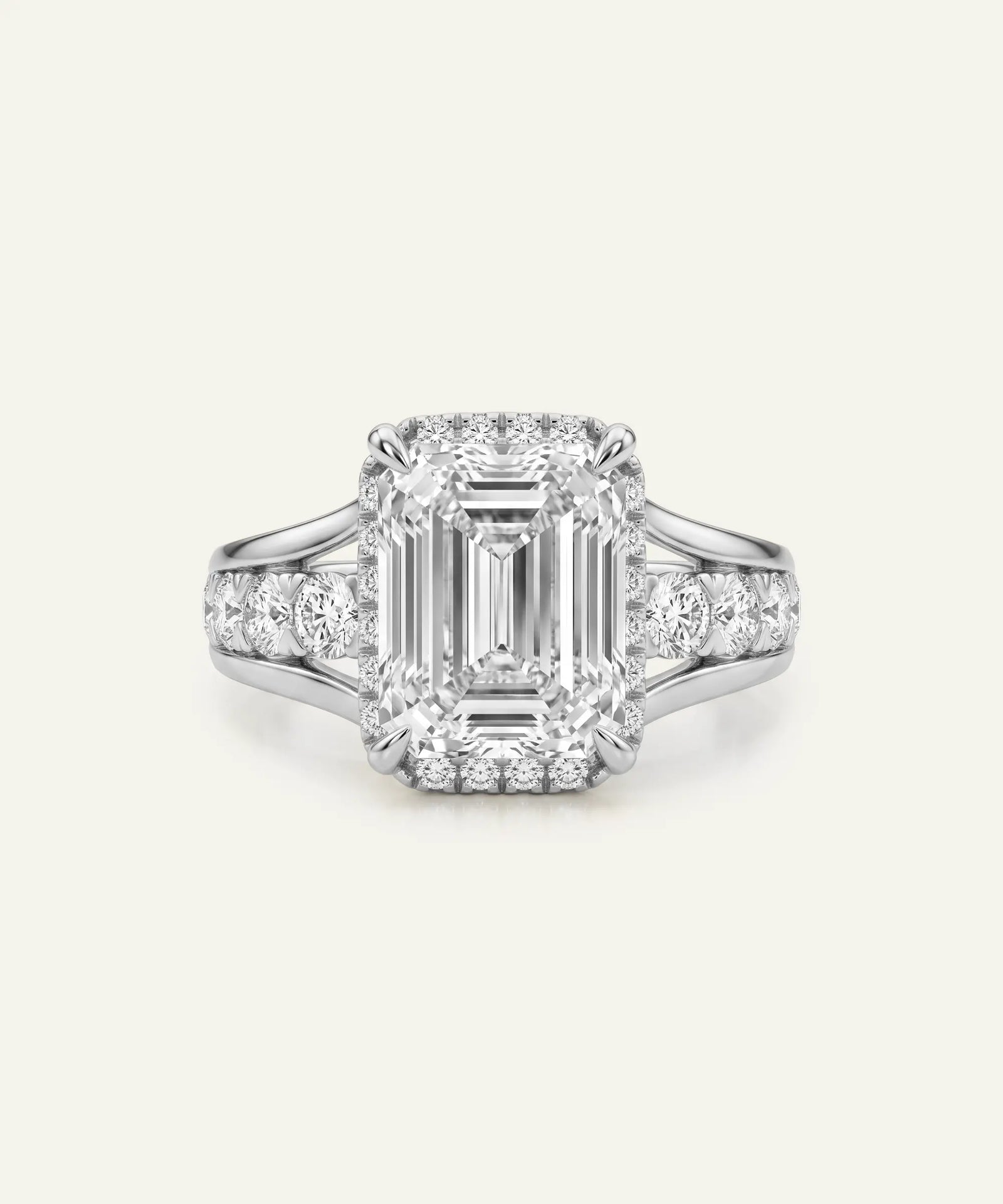 An emerald-cut halo ring in silver-toned metal, featuring a large rectangular baguette center stone surrounded by a double halo and a shank paved with small round stones, set against a solid off-white background.