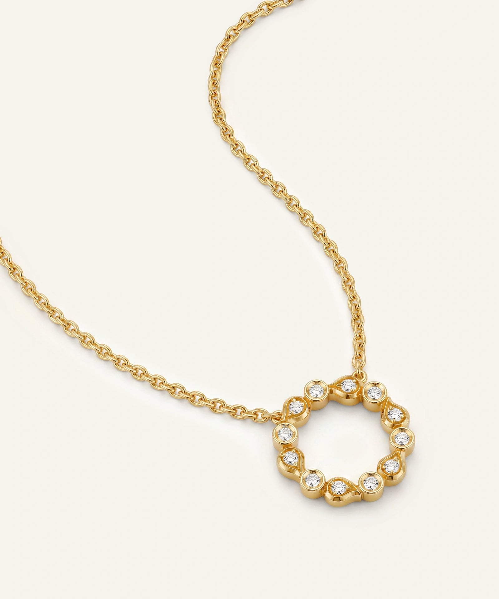 A gold chain necklace featuring a circular open pendant adorned with small clear stones, photographed on a clean off-white background.