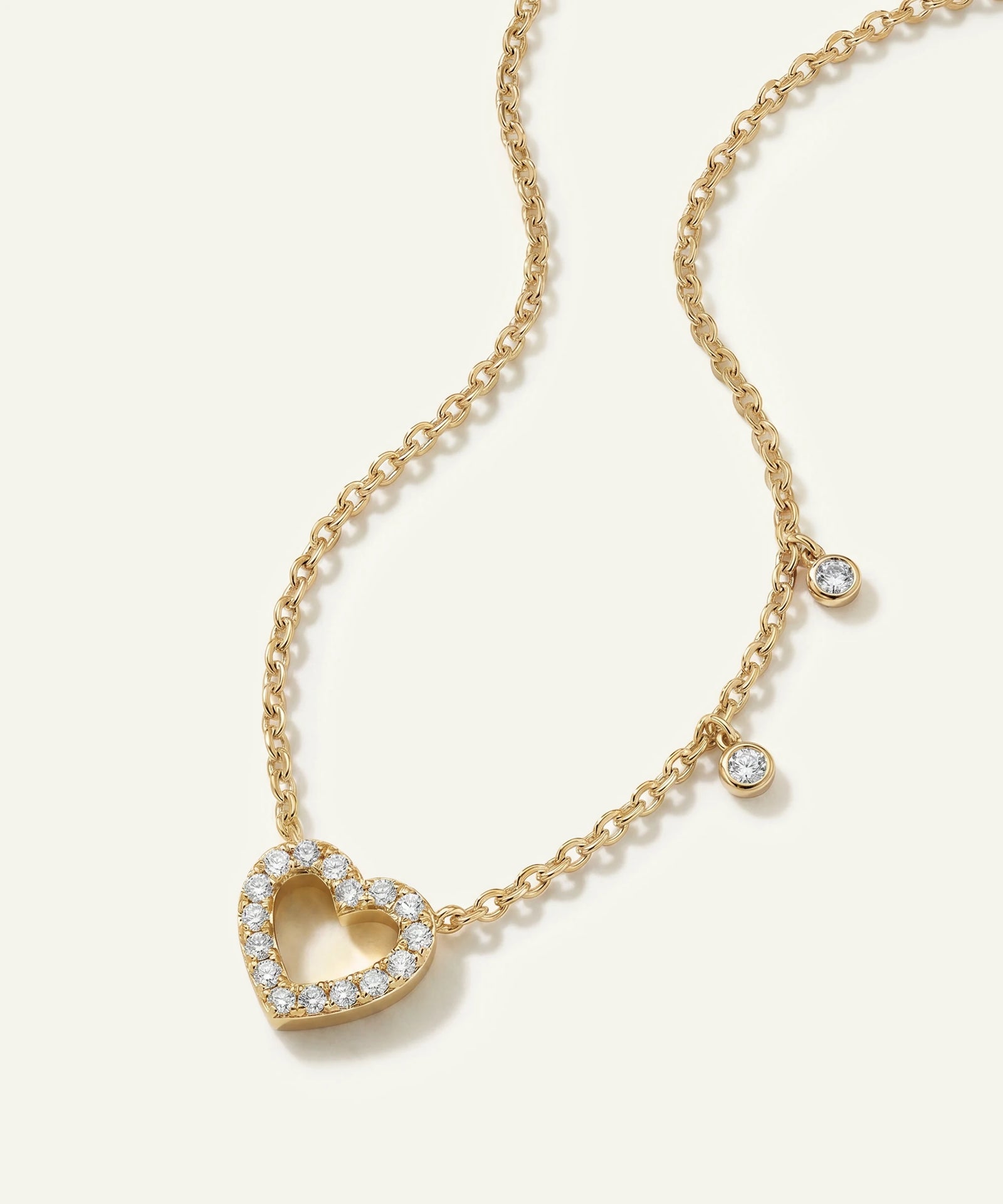 Gold necklace with a heart-shaped pendant on a light beige background