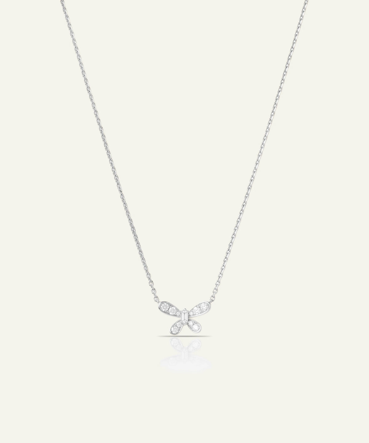 A delicate silver chain necklace featuring a small bow-shaped pendant set with clear gemstones, displayed against a solid off-white background.