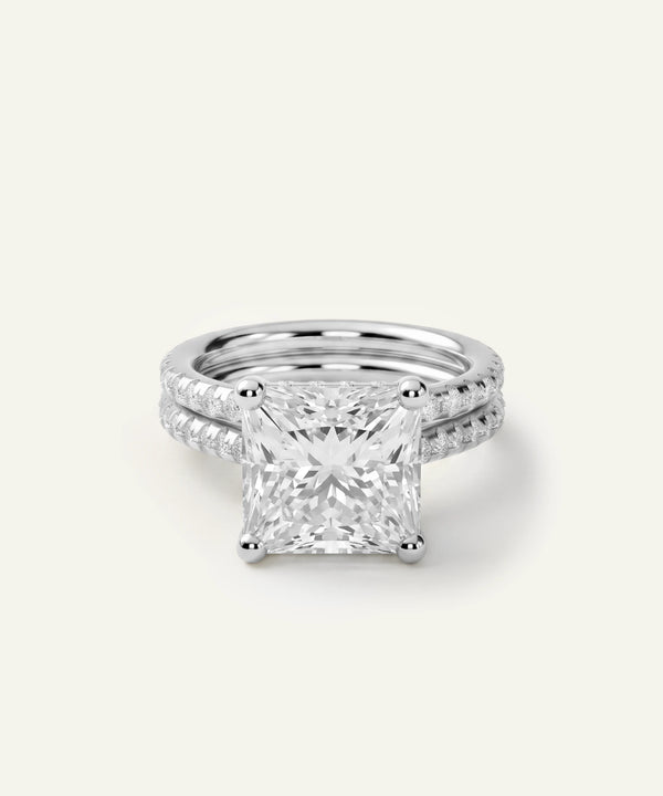 A princess-cut diamond engagement ring with a matching diamond-paved band in a silver-toned setting, photographed on a clean, light off-white background.