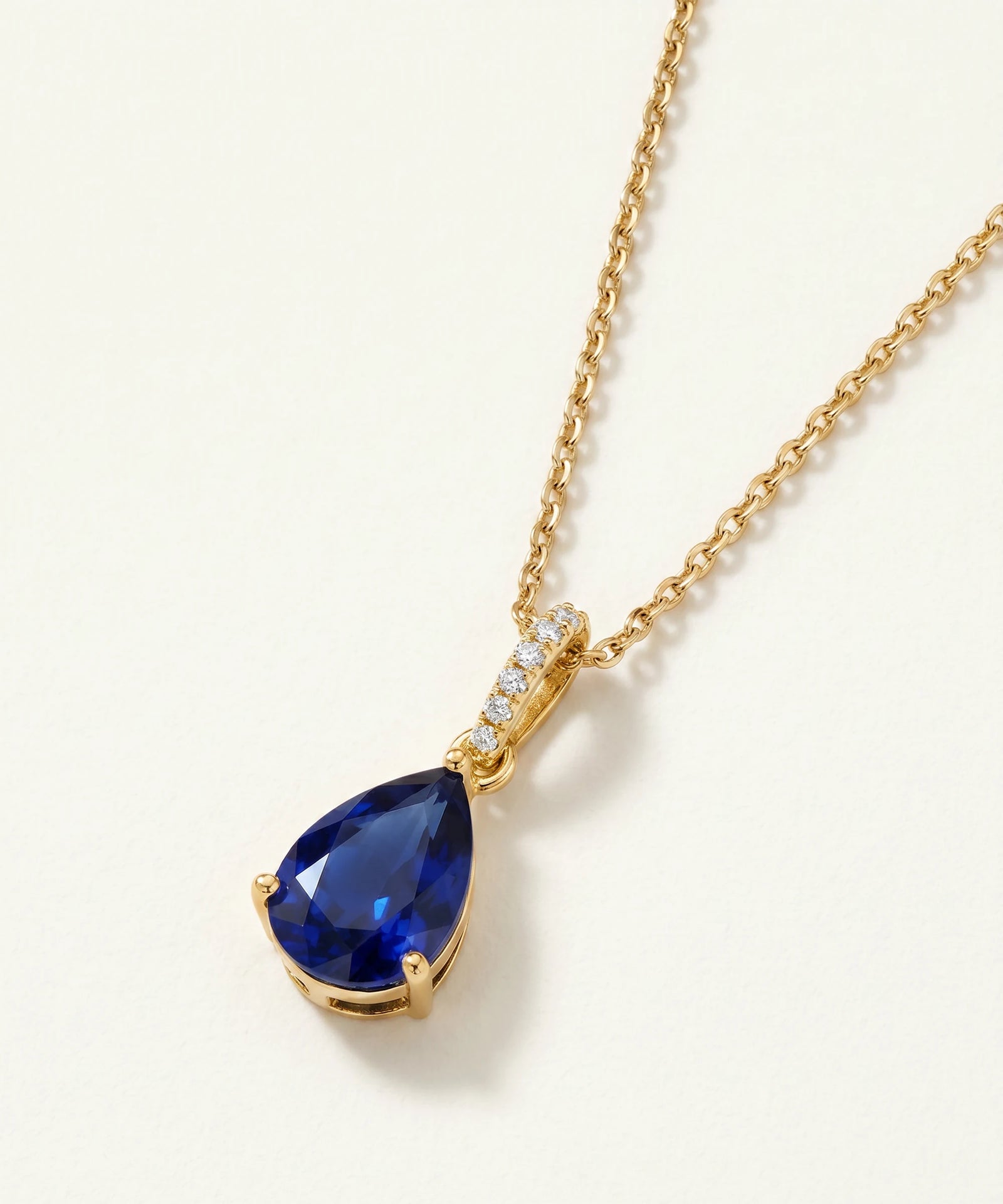 Gold necklace with a blue teardrop pendant on a white background