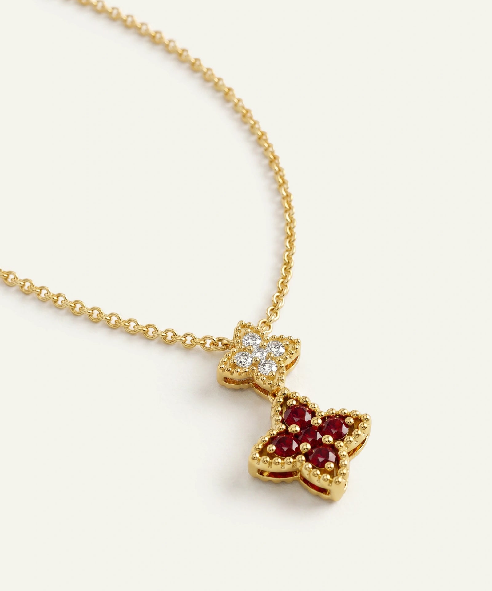 A gold chain necklace with a two-part butterfly pendant. The top butterfly is set with clear cubic zirconia stones, while the larger bottom butterfly is set with round red gemstones and bezel-set gold.