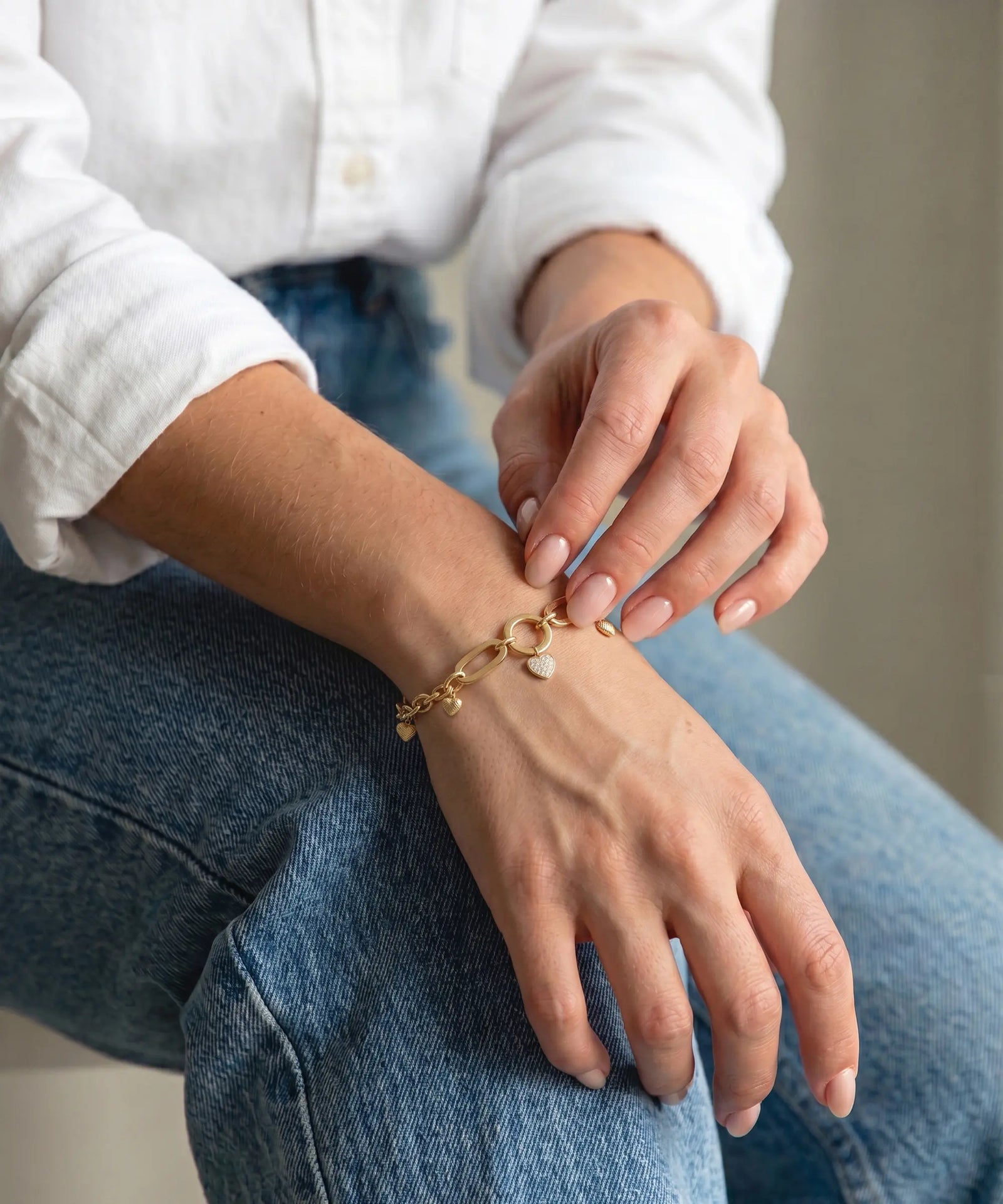 Person wearing gold bracelets on their wrist and hand, sitting on a white surface.