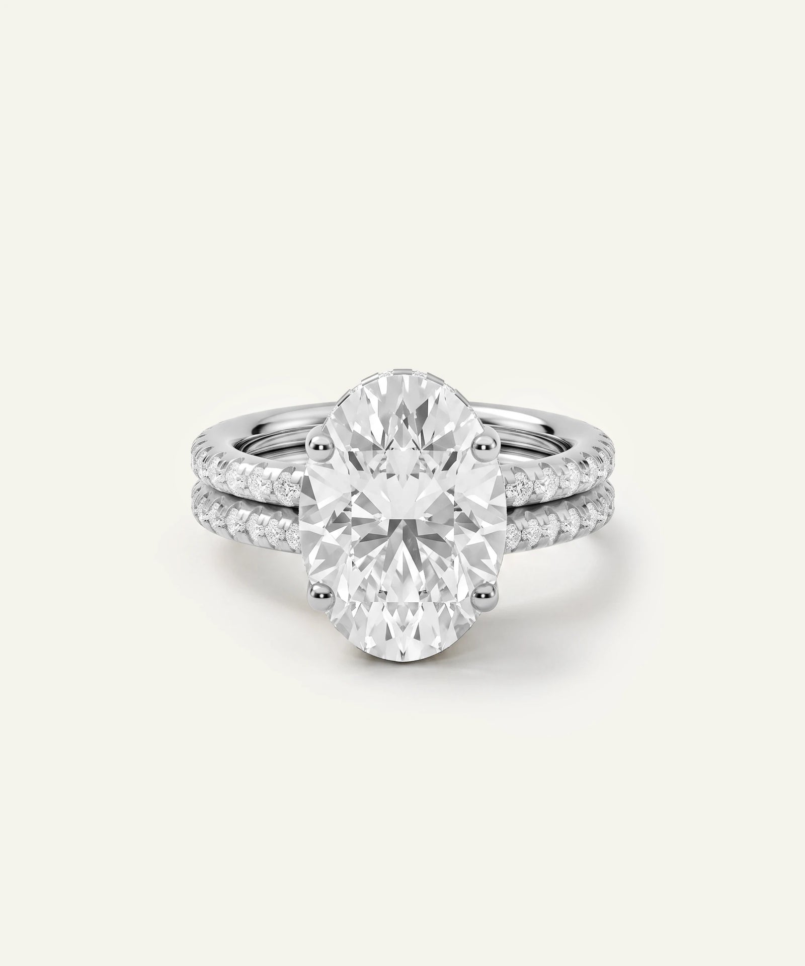 An oval-cut diamond engagement ring with a matching diamond-paved band, set in a silver-colored metal, photographed on a clean, light off-white background.