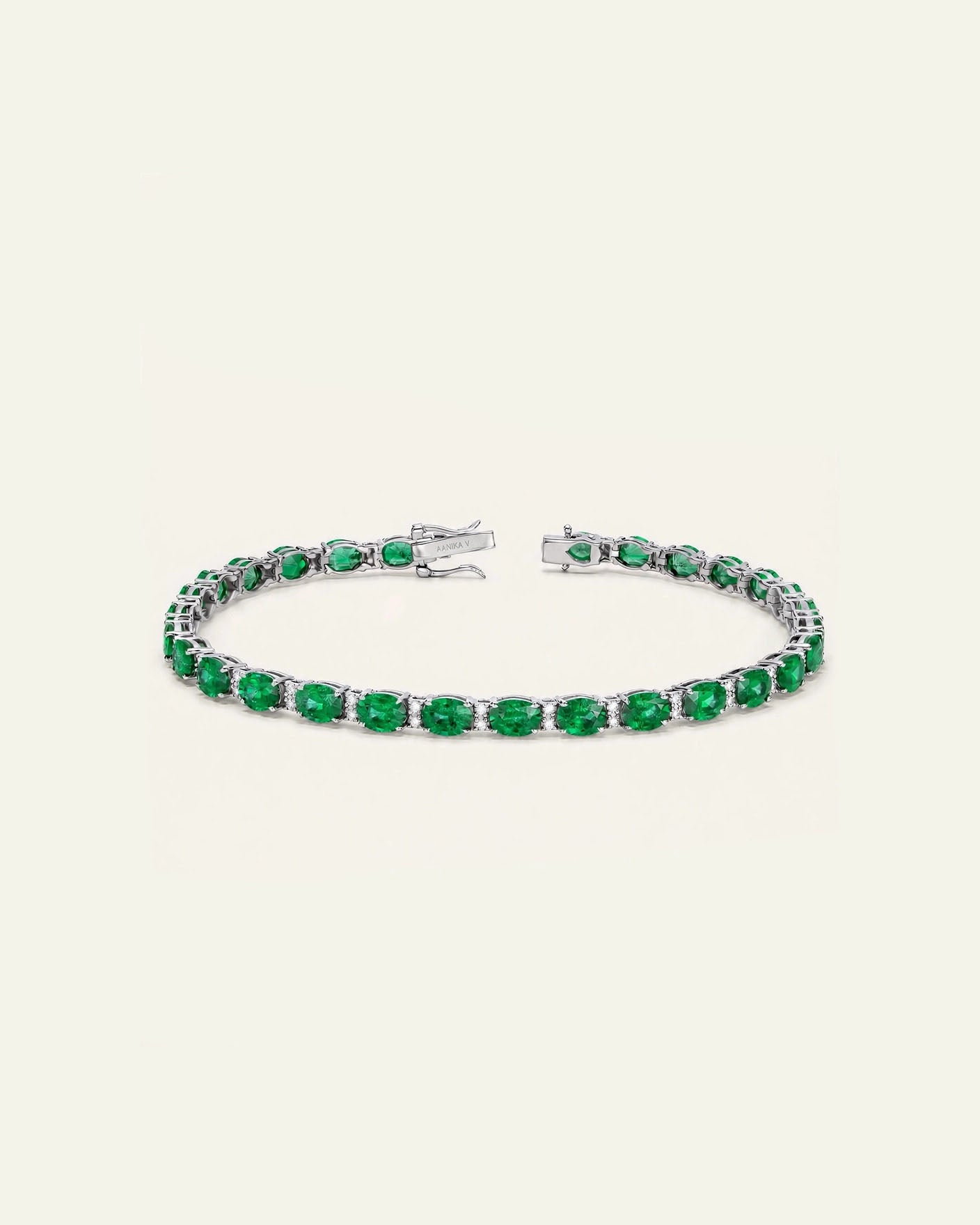 A tennis bracelet featuring round-cut green emeralds in a silver-toned setting, displayed on a light cream background.