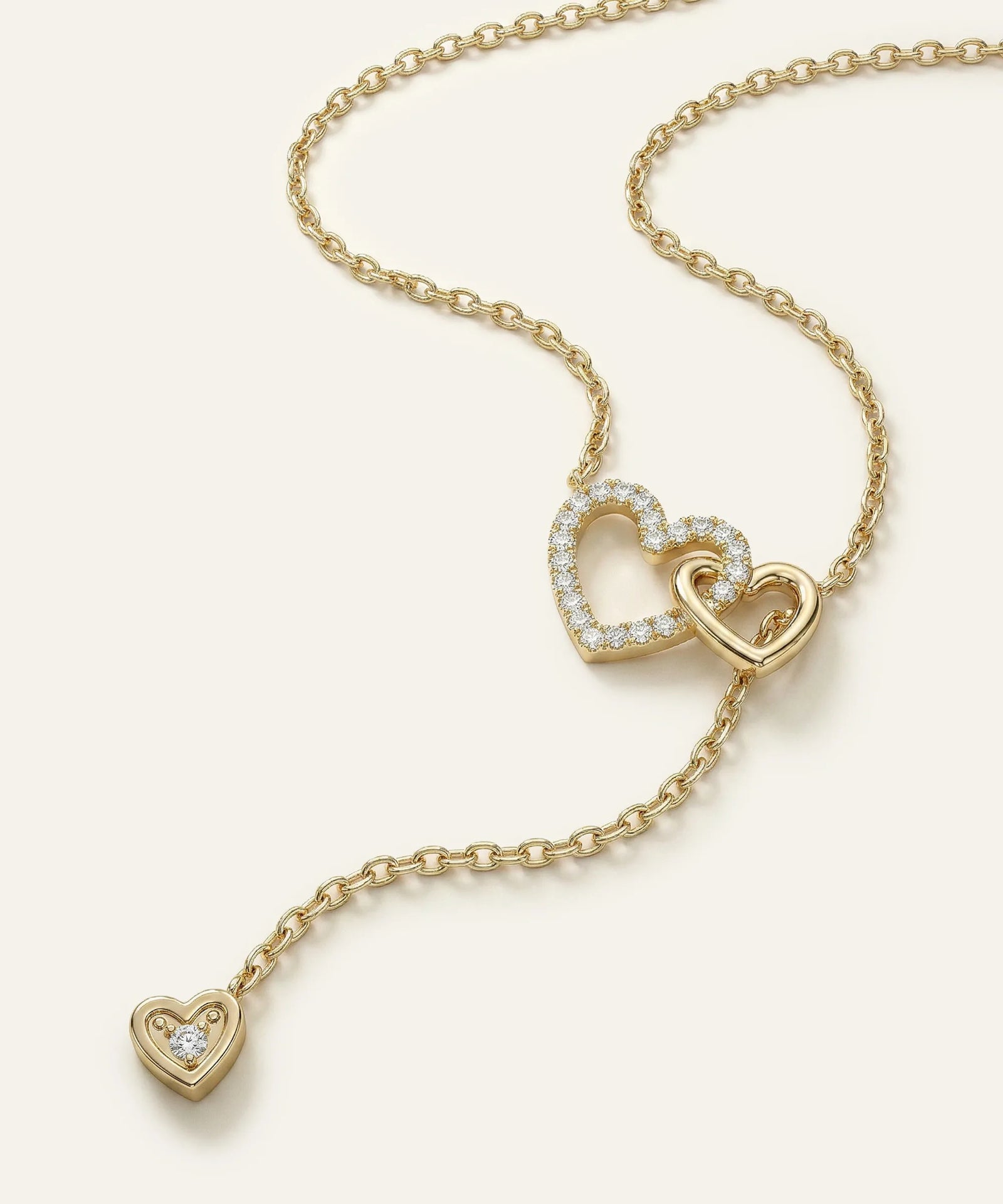 Gold necklace with heart-shaped pendant on a light beige background