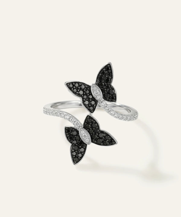 Butterfly-shaped jewelry piece with black and clear gemstones on a light gray background