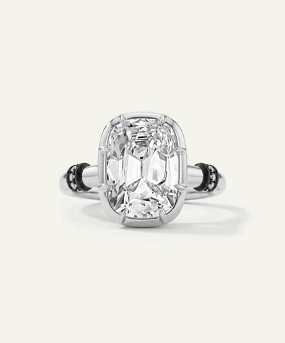 A radiant cut diamond ring with a silver-toned band featuring small black stones on either side, centered on a light cream background. - alternate view