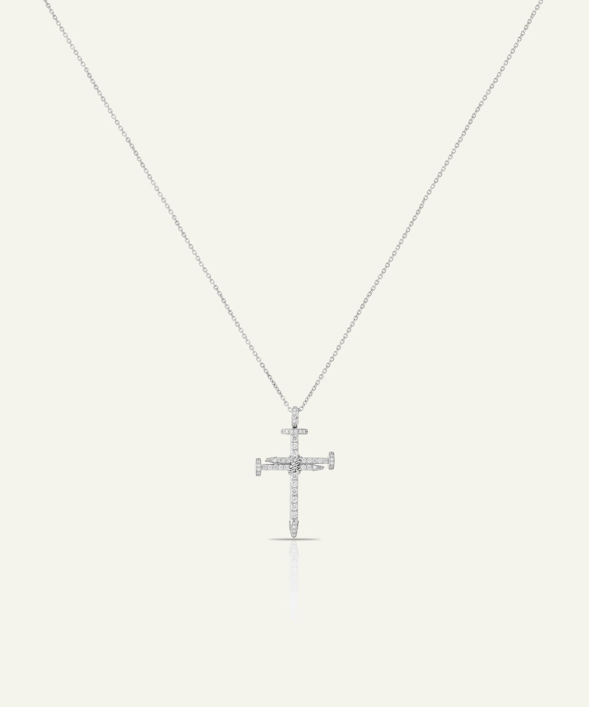 A silver cross pendant necklace with small clear stones, suspended from a delicate silver chain against a light cream background.