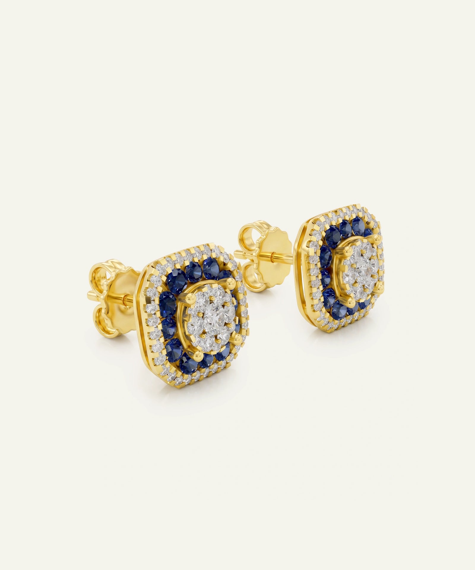 A pair of gold square stud earrings featuring a central round clear stone surrounded by a halo of small clear stones, with a surrounding border of deep blue round stones, set against a plain off-white background.