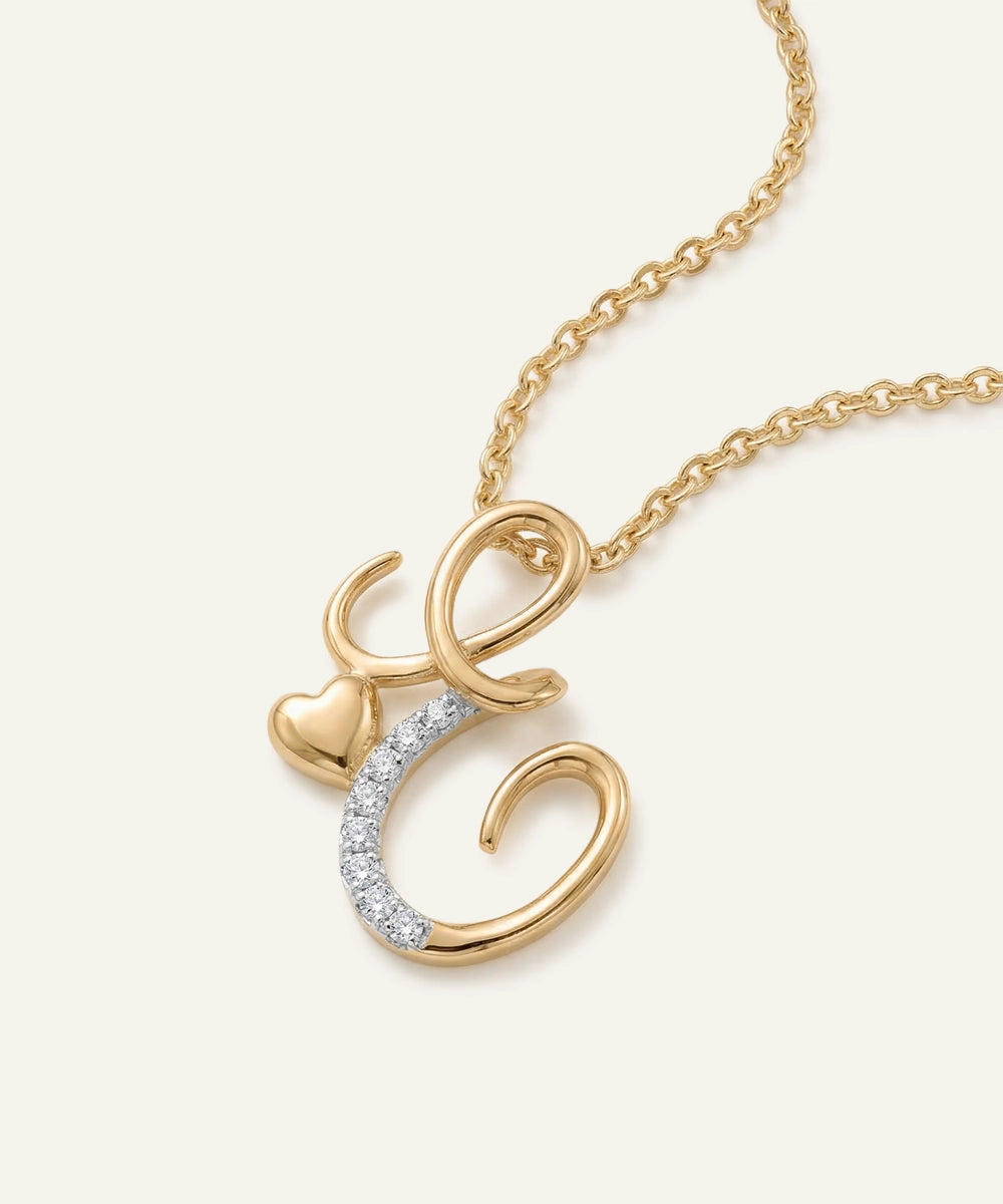 Gold necklace with a heart and letter 'C' pendant on a light beige background