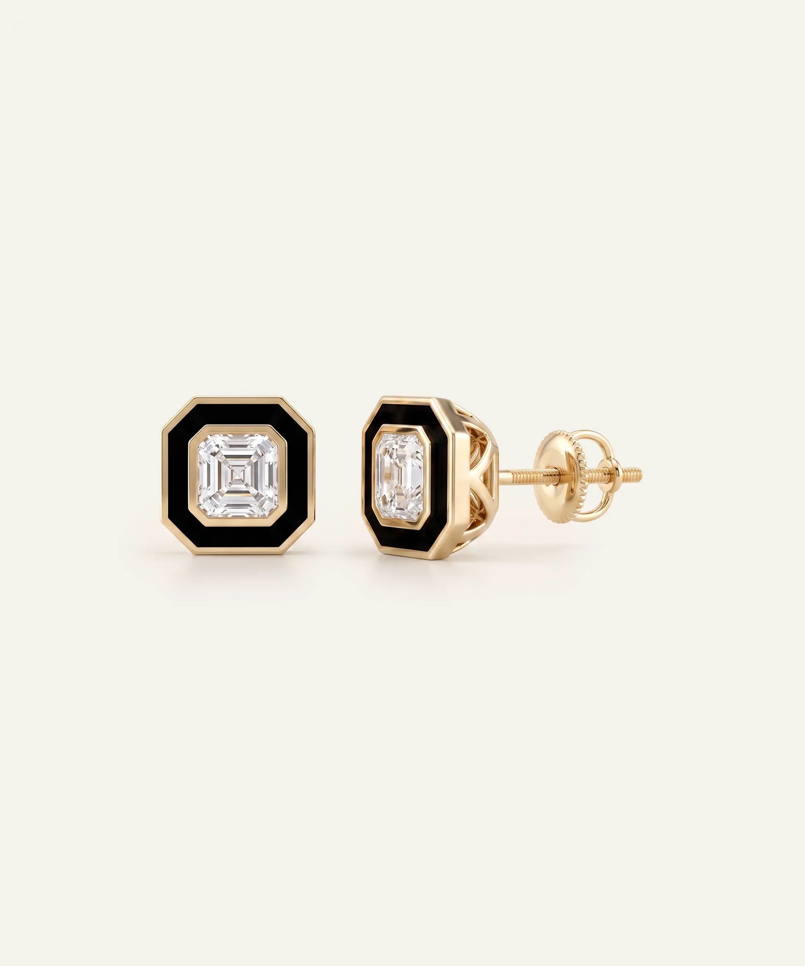 A pair of gold-toned stud earrings with black octagonal inlays and a central clear baguette-cut gemstone, shown on a light cream background.