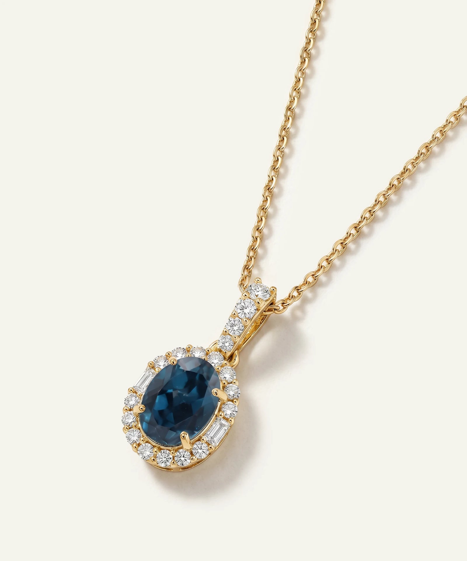 Gold necklace with a blue gemstone pendant on a white background