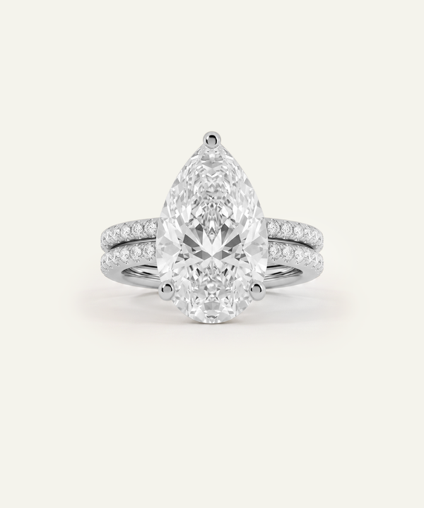 A pear-cut diamond engagement ring with a matching pear-shaped center stone and a slim pavé band, shown on a clean off-white background.