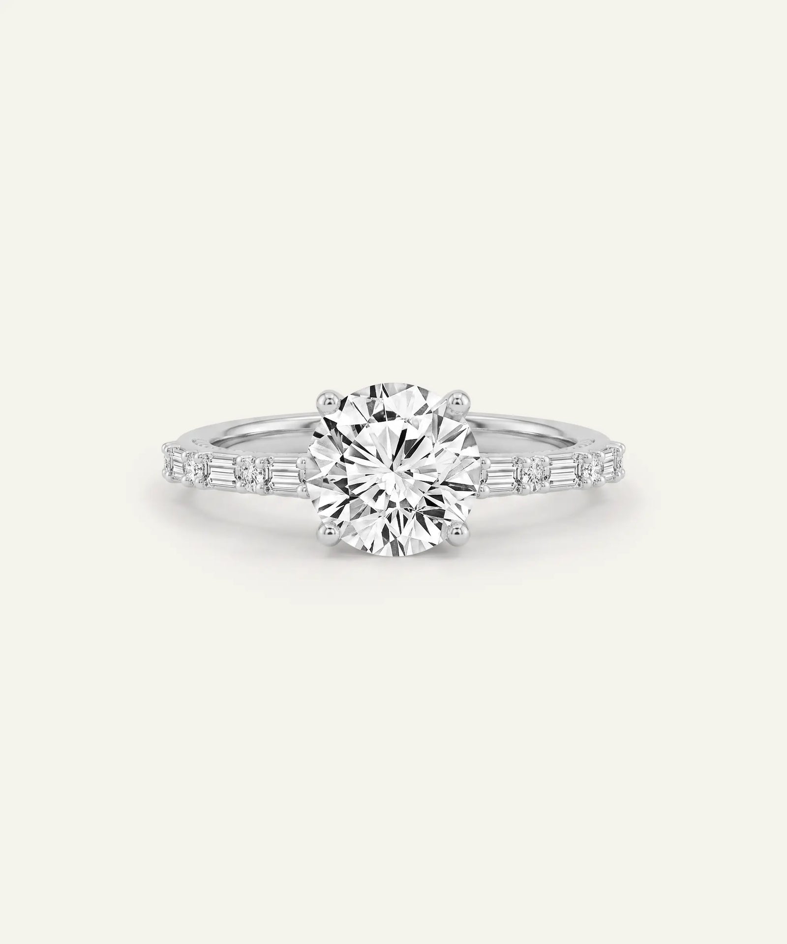 A silver solitaire engagement ring featuring a round brilliant-cut center stone and baguette side stones on a clean, light off-white background.