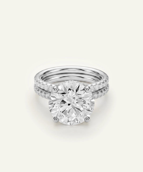 A radiant diamond solitaire ring with a halo setting, shown with a matching pavé band ring behind it on a light cream background.
