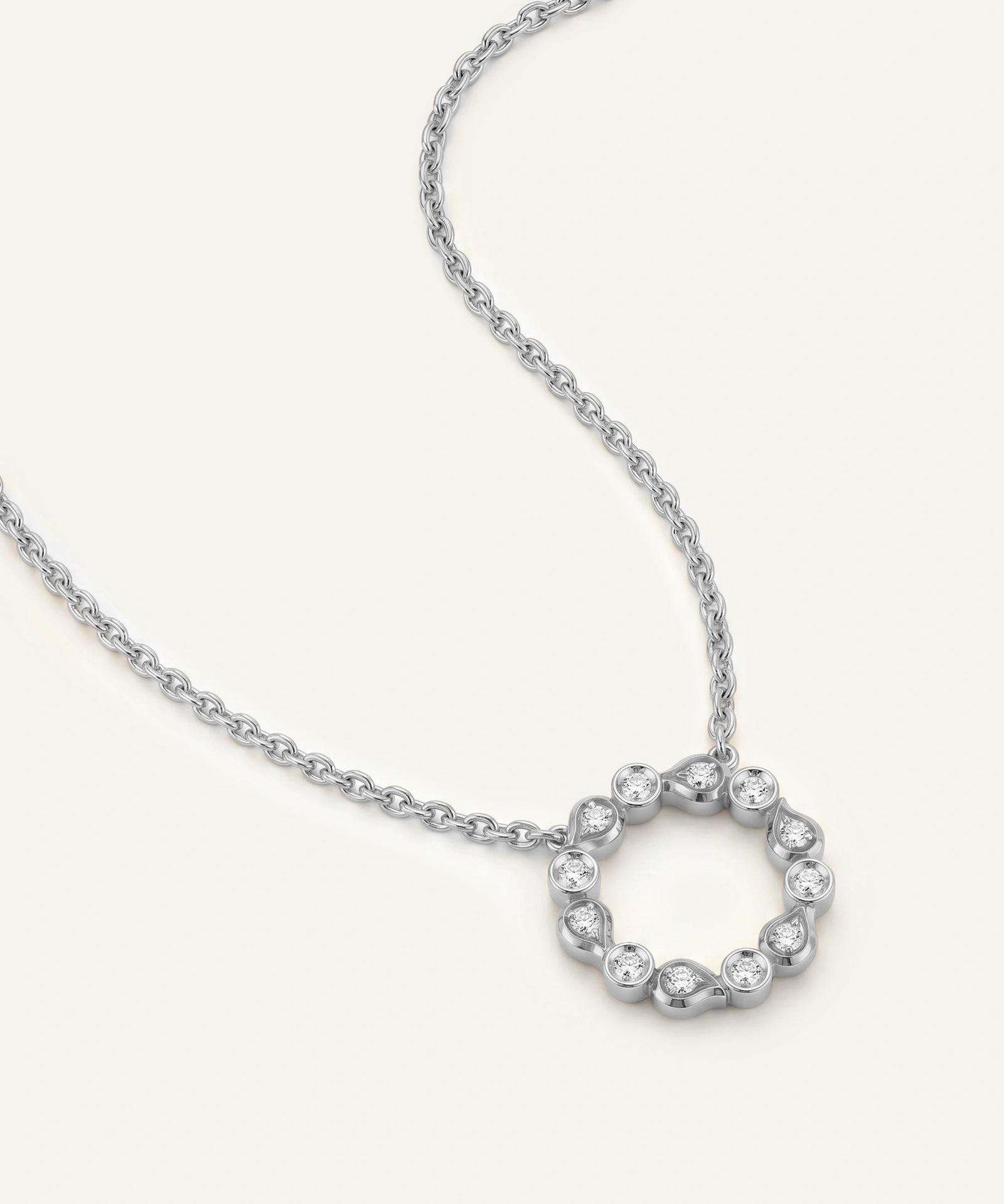 A gold chain necklace featuring a circular open pendant adorned with small clear stones, photographed on a clean off-white background.