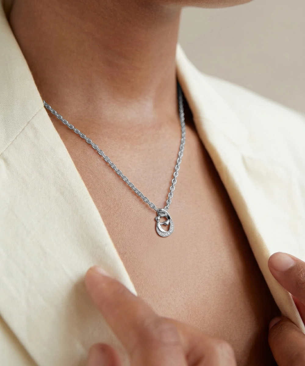 Silver necklace with a pendant worn by a person in a beige outfit.