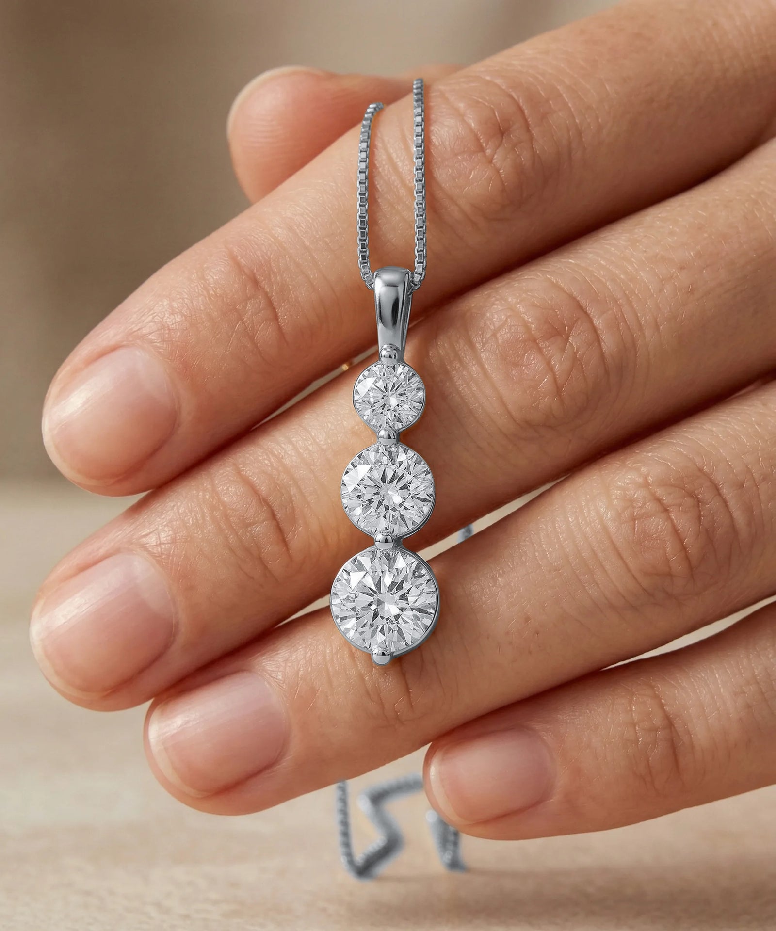 Diamond necklace held by a hand against a neutral background