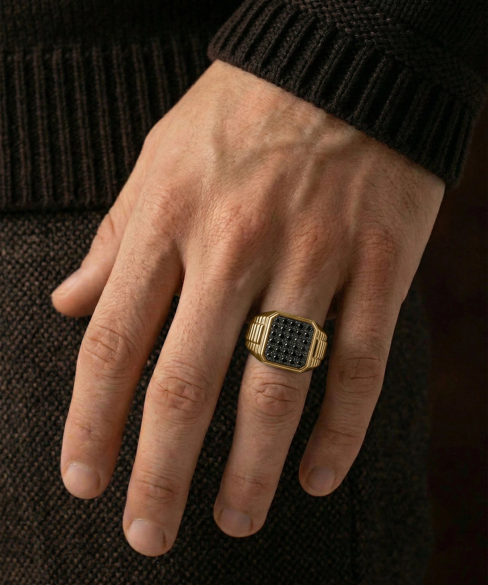 Hand wearing a gold ring with black stones on a dark background