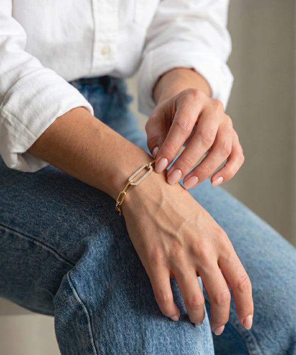 Person wearing gold bracelets on their wrist and hand, sitting on a white surface.