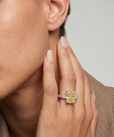 Close-up of a hand wearing a yellow diamond ring with a neutral background - alternate view