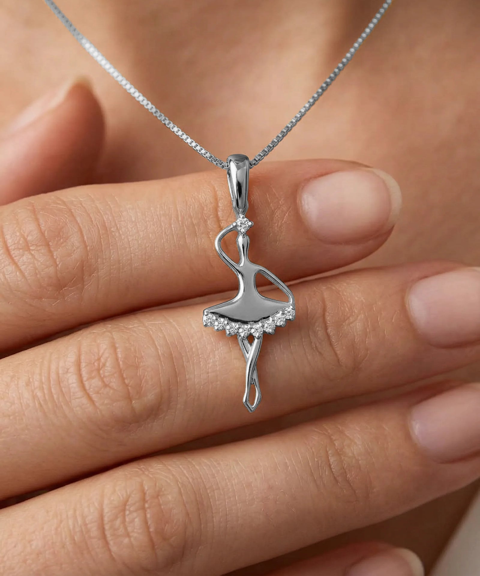Silver ballerina pendant on a chain held between fingers