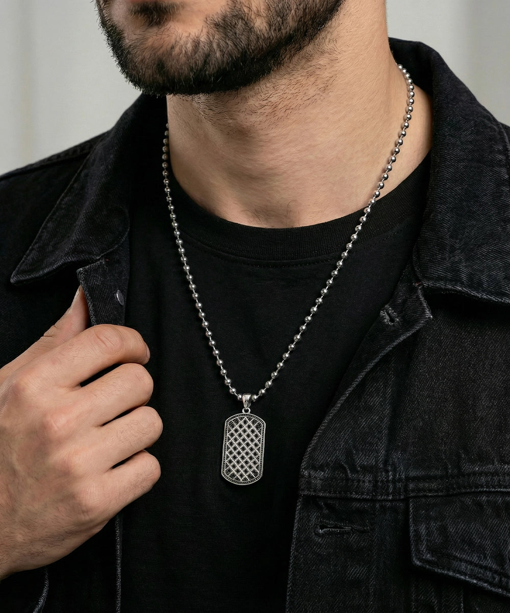 Man wearing a black jacket with a silver chain and dog tag necklace.