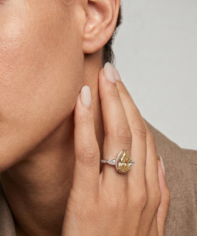 Close-up of a hand wearing a yellow diamond ring with a neutral background - alternate view