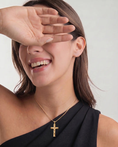 Woman wearing a gold necklace with a cross pendant, covering her eyes with her hand. - alternate view