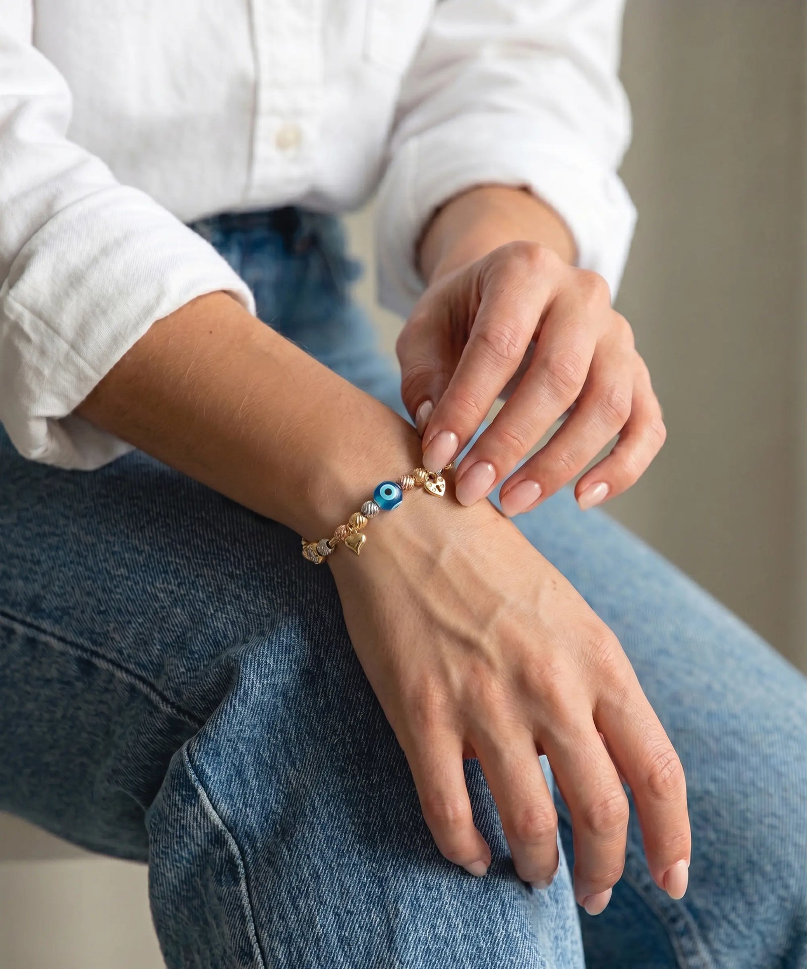 gold evil eye charm bracelet with heart charms, styled on a wrist.