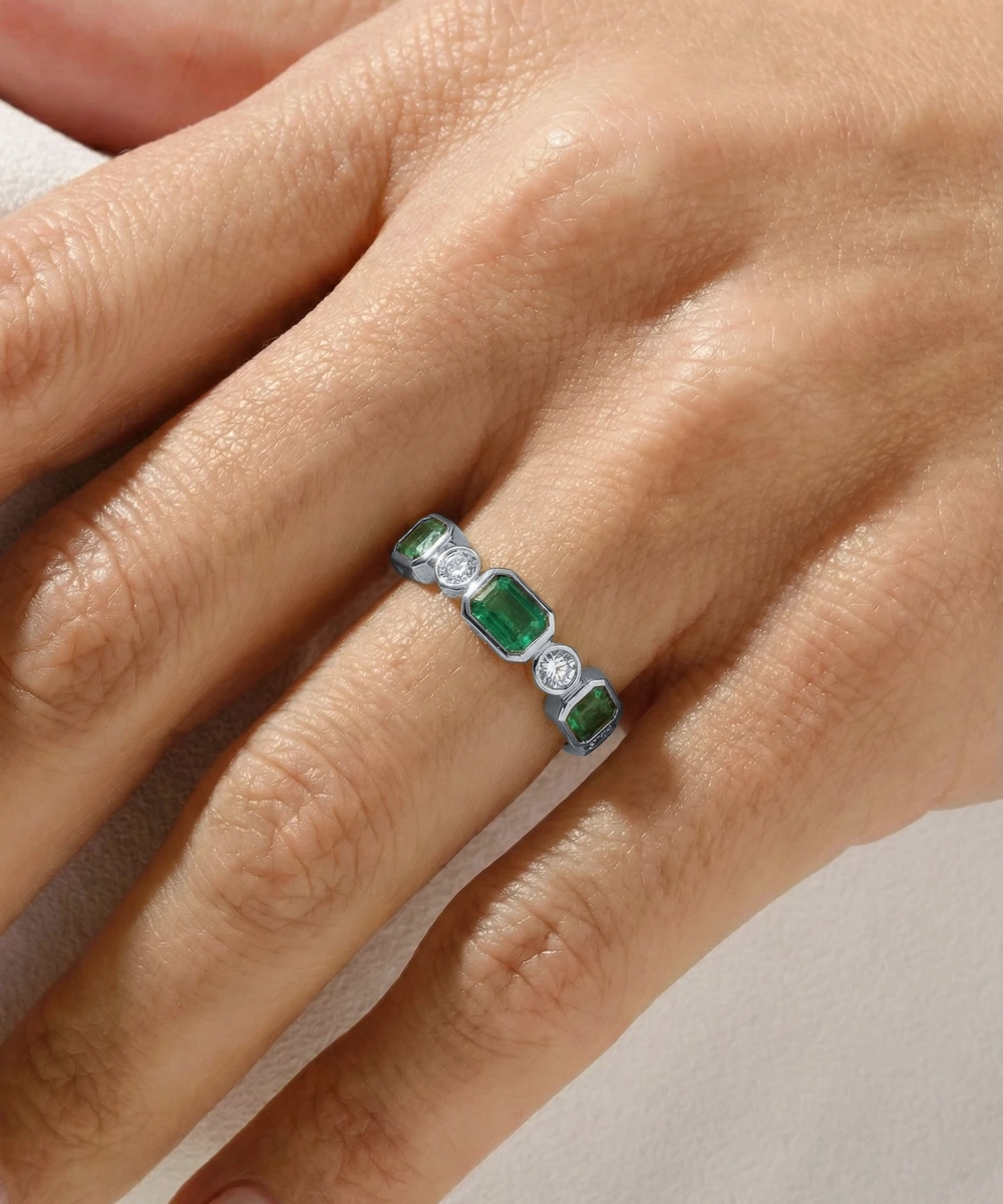Ring with emeralds and diamonds on a hand against a neutral background
