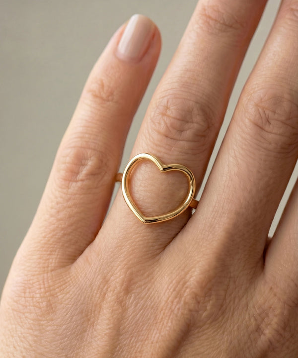 Gold heart-shaped ring on a person's finger against a neutral background