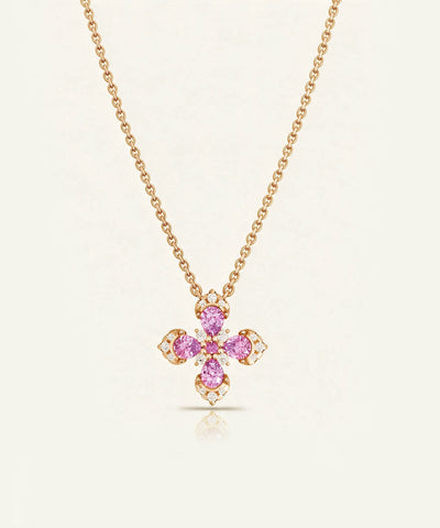 A gold chain necklace with a four-petal cross pendant featuring pink gemstones and small clear accent stones, displayed on a light cream background.