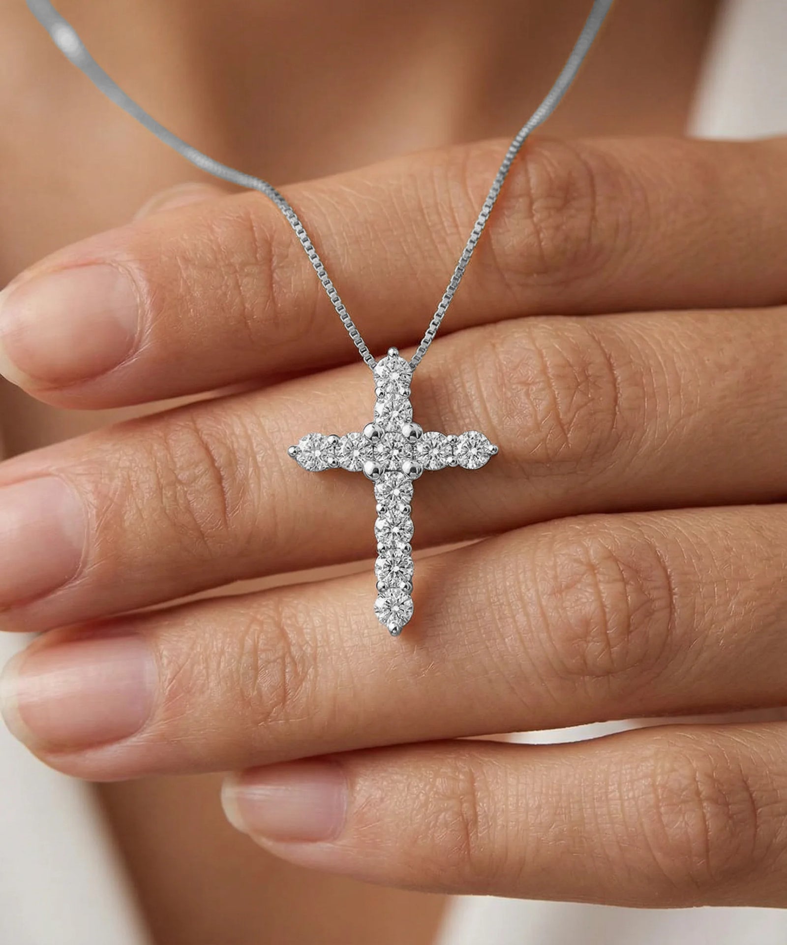Silver cross necklace with diamonds held between fingers
