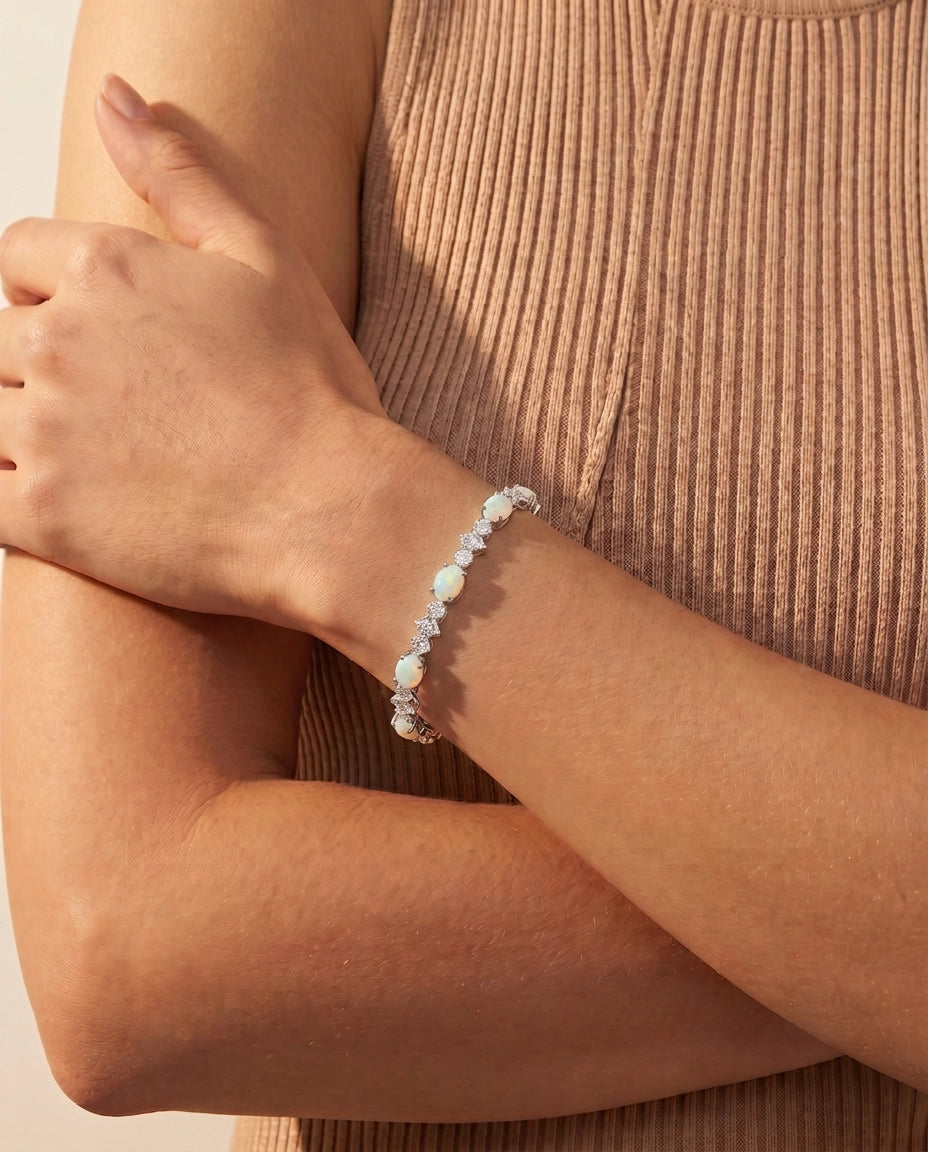 A close-up of a person's forearm and hand wearing a delicate beaded bracelet with white and iridescent beads over a ribbed beige top.