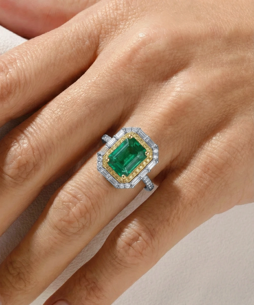 Gold and silver ring with emerald on a hand against a neutral background