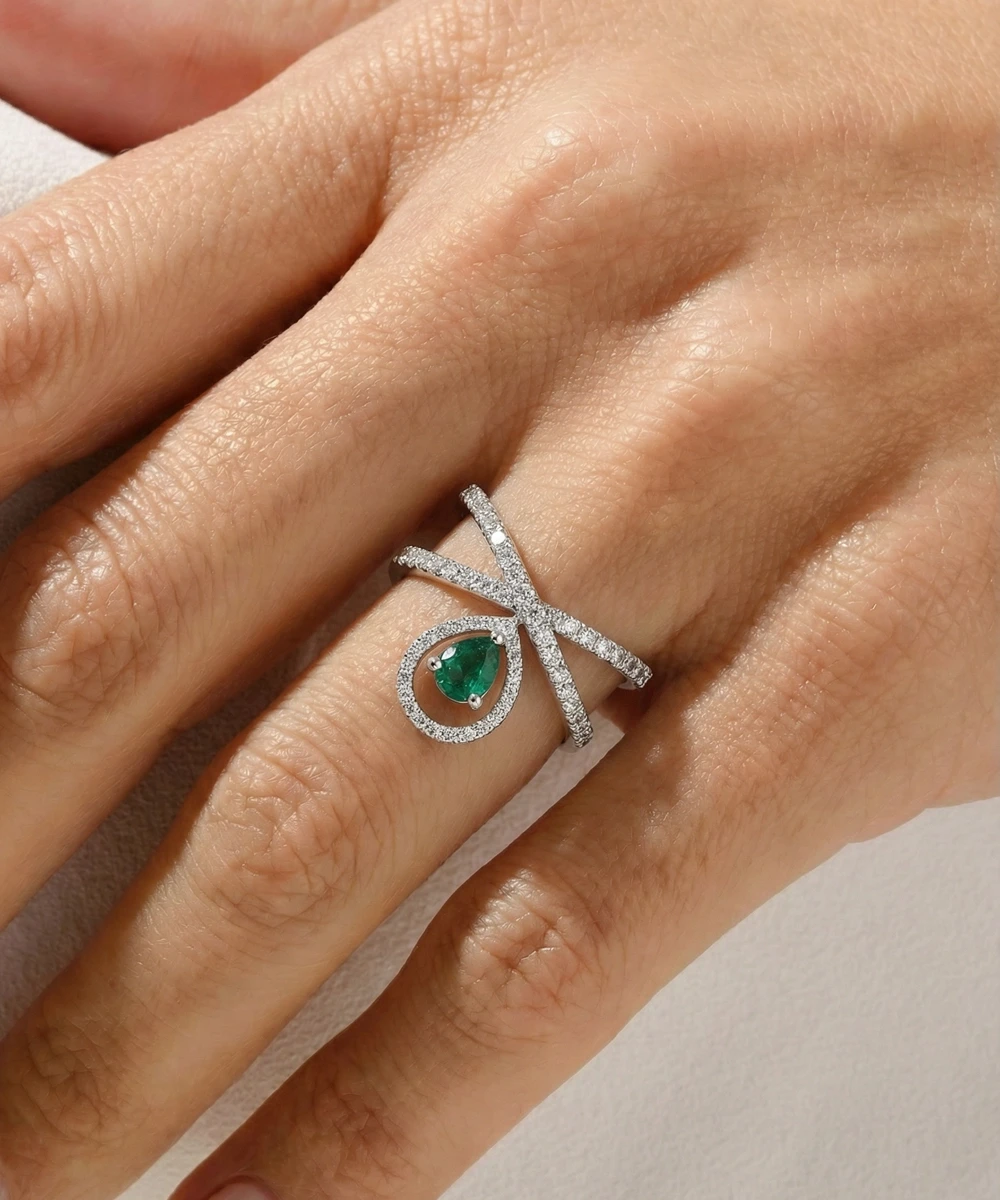 Silver ring with a green gemstone on a hand against a neutral background