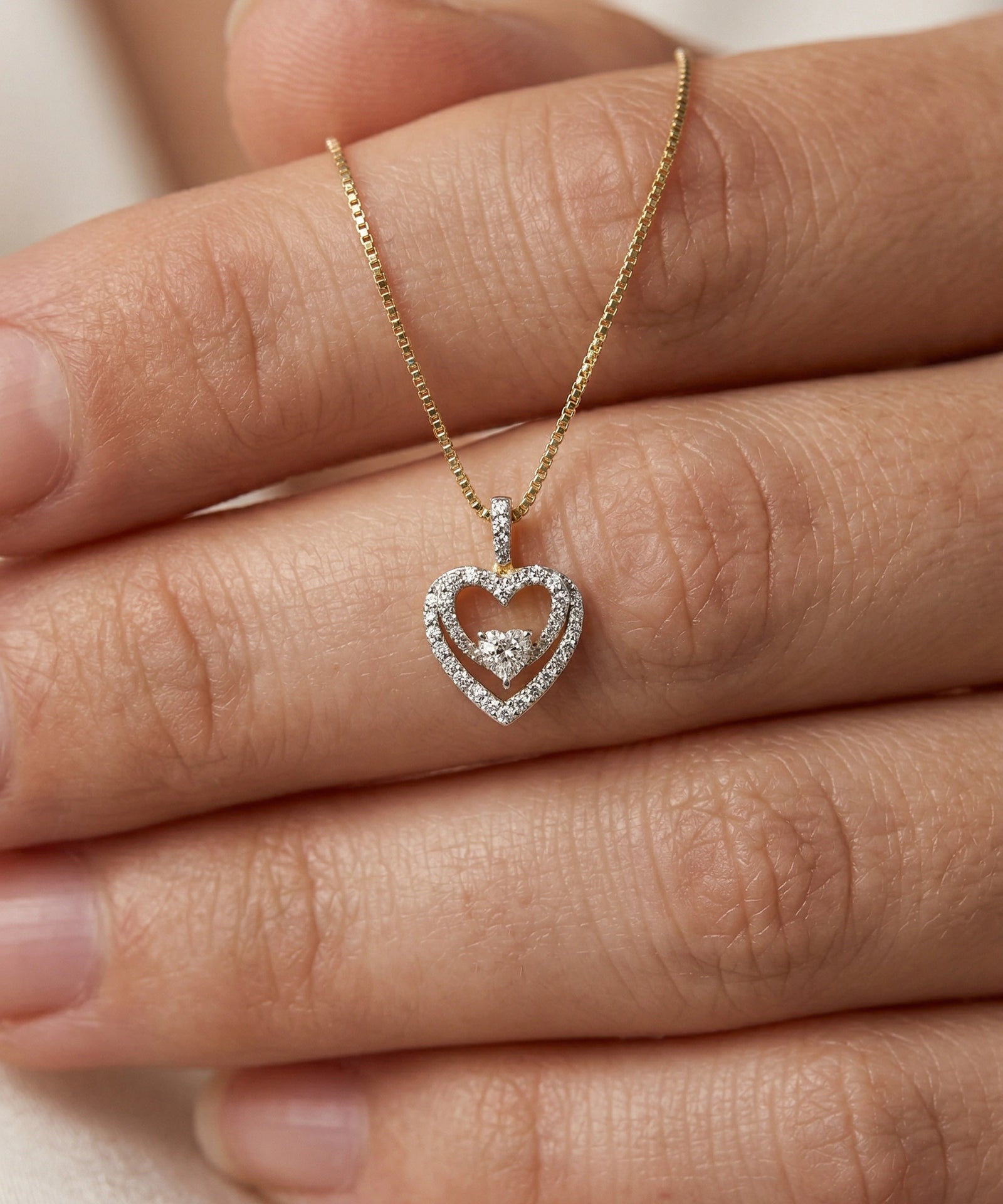 Gold necklace with a heart-shaped pendant on a hand