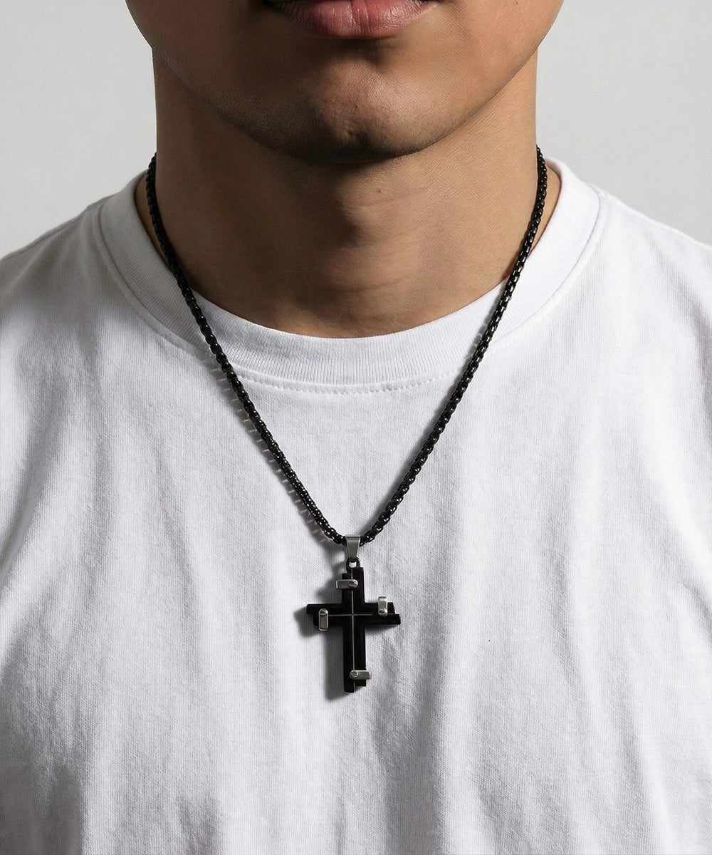Person wearing a black cross necklace on a plain background