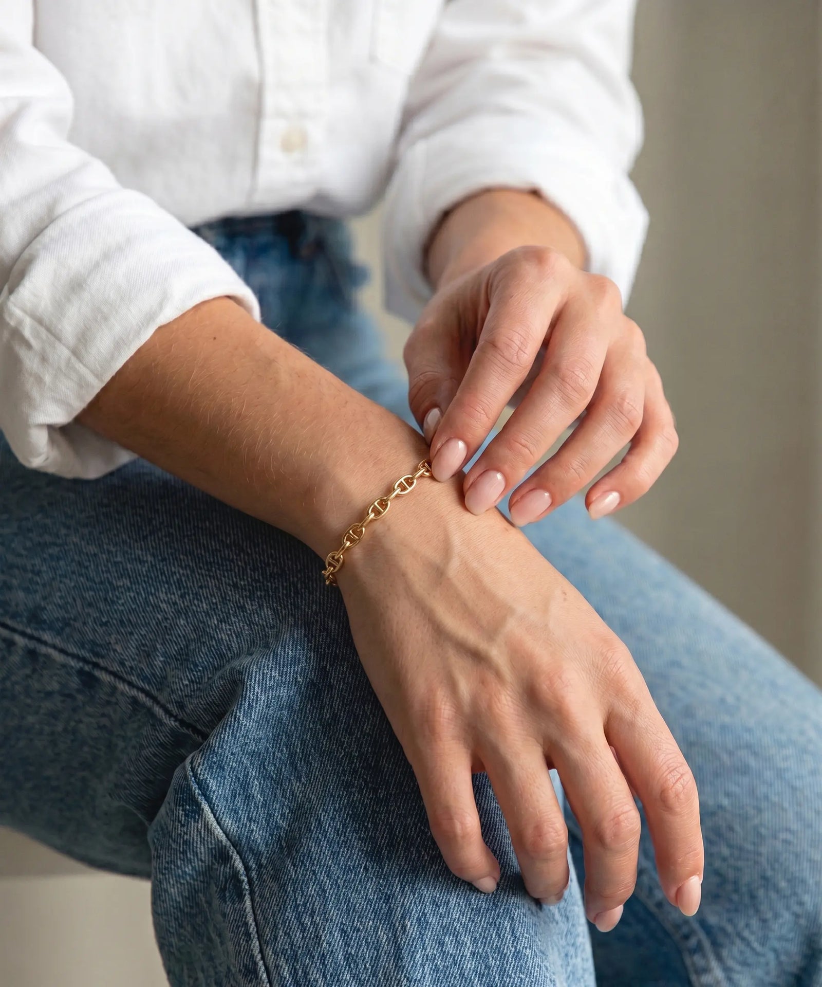 Person wearing gold bracelets on their wrist and hand, sitting on a white surface.