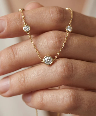 Gold necklace with diamond pendants on a hand against a neutral background - alternate view