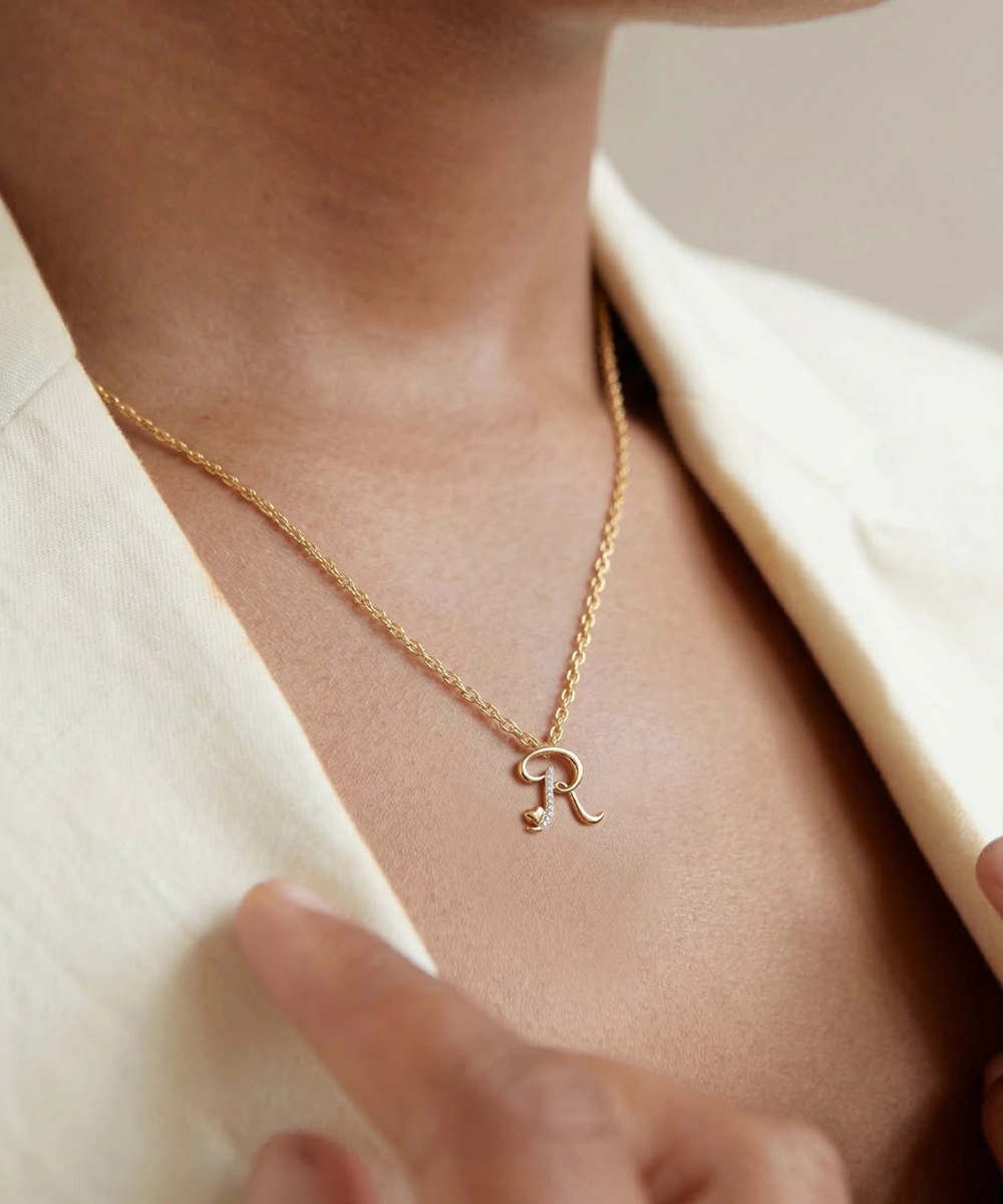 Silver necklace with a letter 'R' pendant on a person wearing a beige blazer.